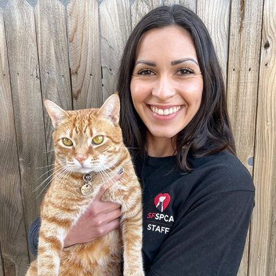 Kylie Ramos in a black SF SPCA t-shirt, smiling and holding an orange cat